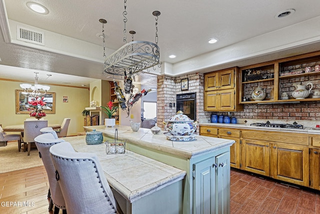 kitchen featuring stainless steel gas stovetop, a center island, hanging light fixtures, tile counters, and dark hardwood / wood-style flooring