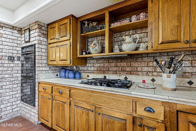 kitchen with stainless steel gas stovetop, dark hardwood / wood-style floors, and brick wall