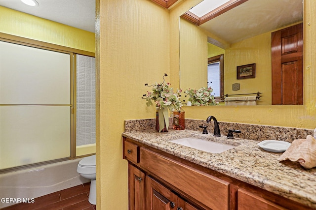 full bathroom with a skylight, vanity, hardwood / wood-style flooring, enclosed tub / shower combo, and toilet