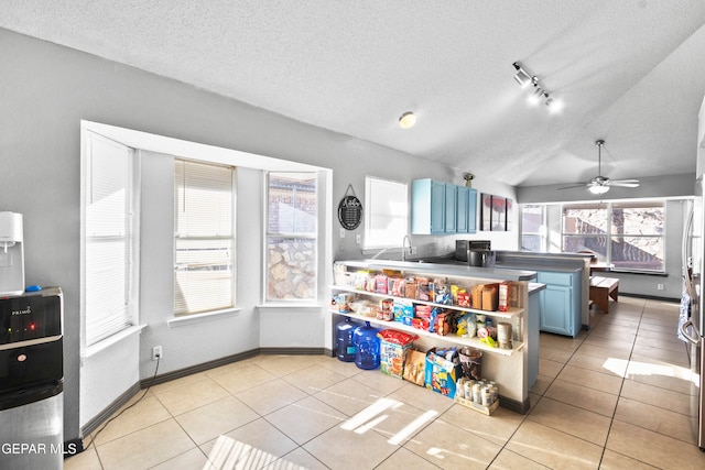 kitchen with track lighting, light tile patterned floors, blue cabinetry, and vaulted ceiling