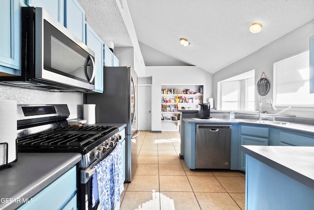 kitchen with blue cabinets, vaulted ceiling, light tile patterned floors, a textured ceiling, and stainless steel appliances