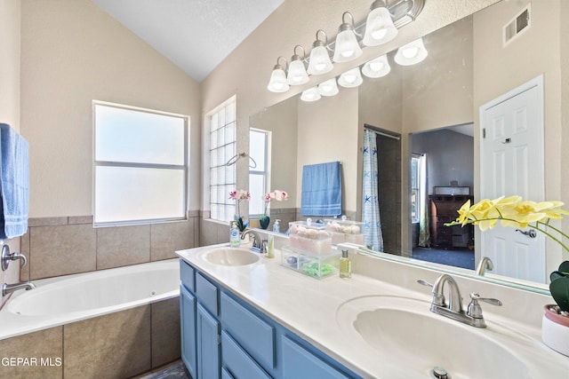 bathroom with vanity, a relaxing tiled tub, lofted ceiling, and a textured ceiling