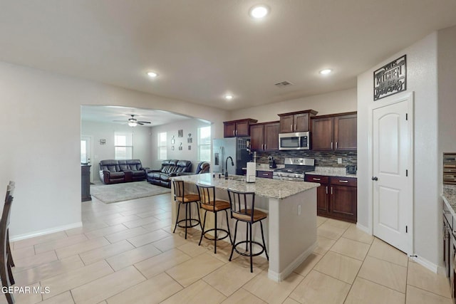 kitchen with a kitchen island with sink, ceiling fan, appliances with stainless steel finishes, tasteful backsplash, and a breakfast bar area