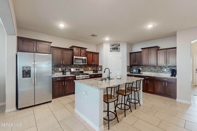 kitchen with tasteful backsplash, sink, a center island with sink, and appliances with stainless steel finishes