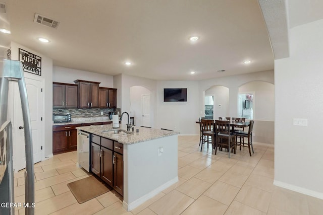 kitchen featuring light stone countertops, backsplash, sink, dishwasher, and an island with sink