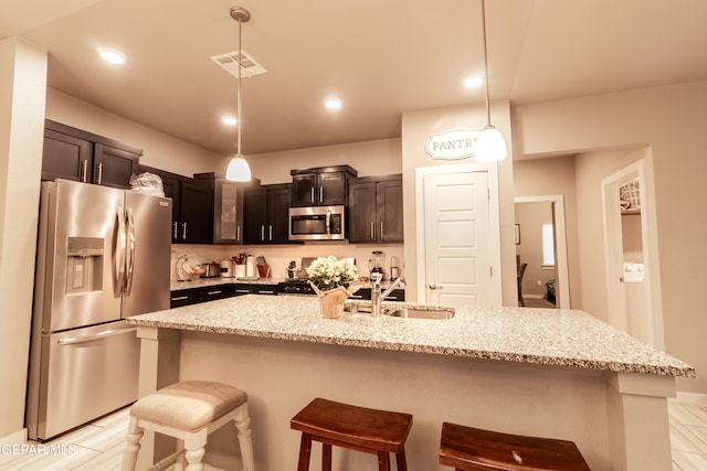 kitchen with decorative light fixtures, a kitchen island with sink, stainless steel appliances, and a breakfast bar