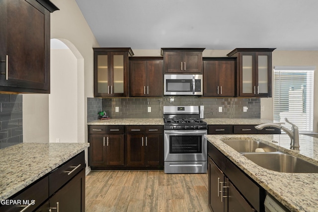 kitchen featuring sink, light hardwood / wood-style flooring, decorative backsplash, dark brown cabinets, and appliances with stainless steel finishes