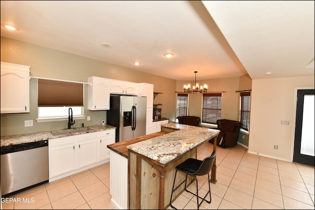 kitchen with sink, stainless steel appliances, a kitchen island, decorative light fixtures, and white cabinets