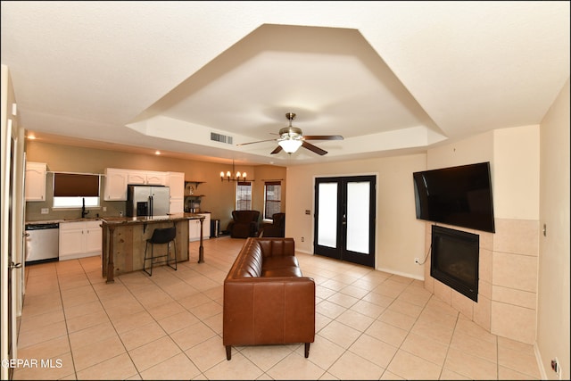 living room featuring a tile fireplace, french doors, ceiling fan with notable chandelier, and a raised ceiling