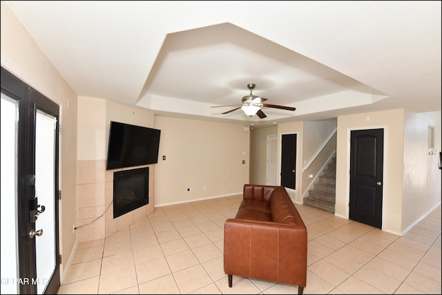 living room featuring ceiling fan, light tile patterned floors, a tile fireplace, and a tray ceiling