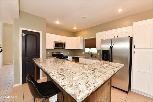 kitchen featuring white cabinets, light stone counters, a kitchen island, and stainless steel appliances