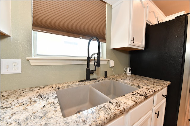 kitchen featuring light stone countertops, sink, black refrigerator, white cabinets, and wood ceiling