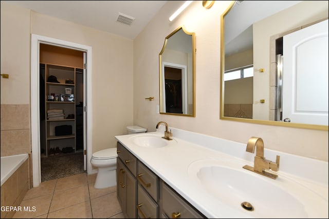 bathroom with tile patterned flooring, vanity, tiled bath, and toilet