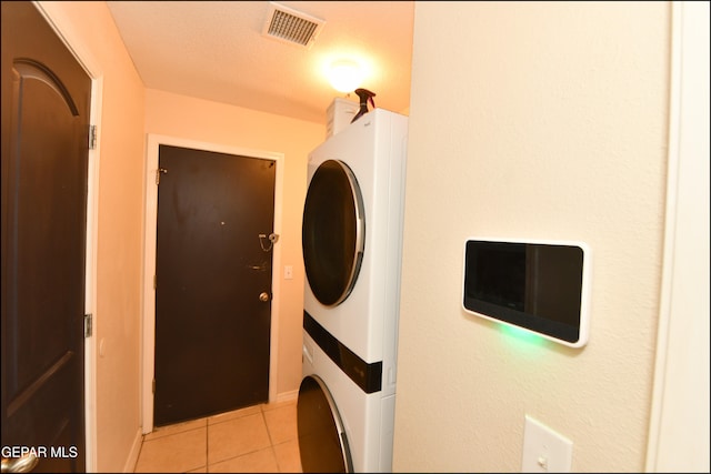 washroom featuring stacked washing maching and dryer, a textured ceiling, and light tile patterned floors