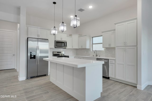 kitchen featuring sink, appliances with stainless steel finishes, white cabinetry, hanging light fixtures, and a center island