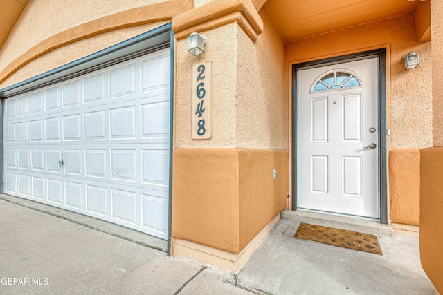 view of exterior entry with a garage and stucco siding