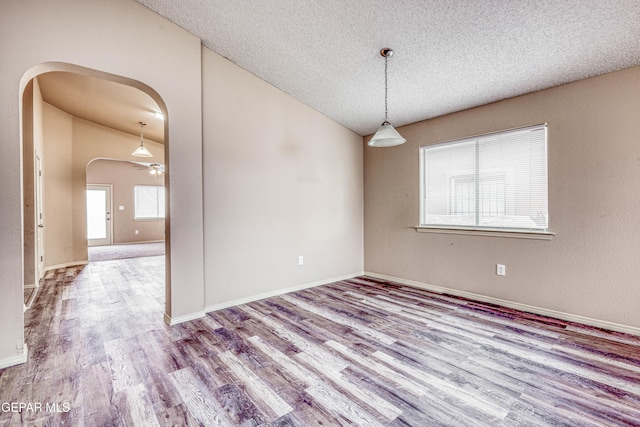 empty room with arched walkways, a textured ceiling, lofted ceiling, wood finished floors, and baseboards