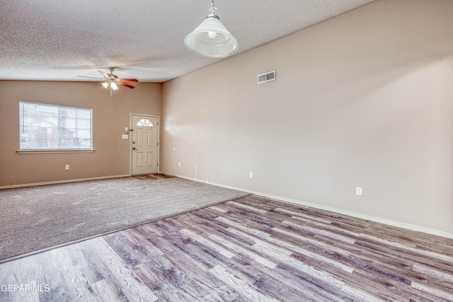 unfurnished room with lofted ceiling, a textured ceiling, wood finished floors, visible vents, and baseboards