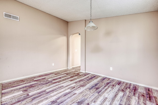 empty room with arched walkways, a textured ceiling, wood finished floors, visible vents, and baseboards