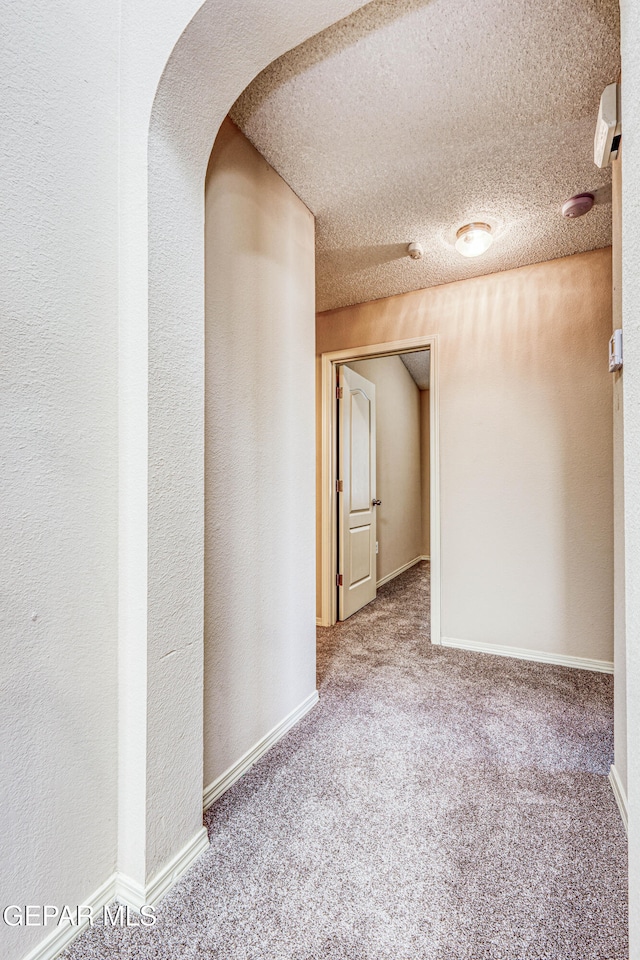 carpeted empty room featuring a textured ceiling, a textured wall, and baseboards