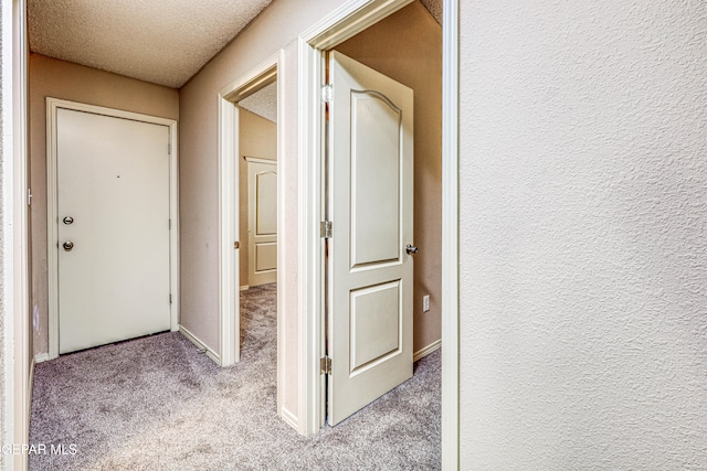 hallway with a textured wall, a textured ceiling, and light colored carpet