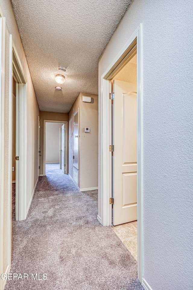 hallway featuring a textured ceiling, a textured wall, carpet flooring, and baseboards