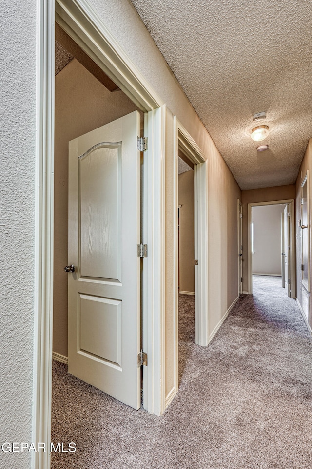 corridor with a textured ceiling, baseboards, carpet flooring, and a textured wall