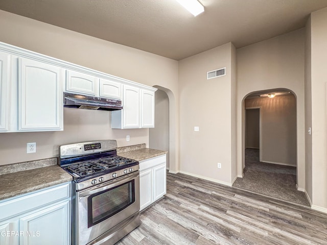 kitchen featuring arched walkways, under cabinet range hood, visible vents, white cabinets, and gas stove