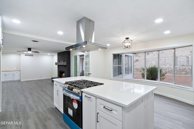 kitchen featuring island range hood, ceiling fan with notable chandelier, a fireplace, gas stove, and white cabinetry