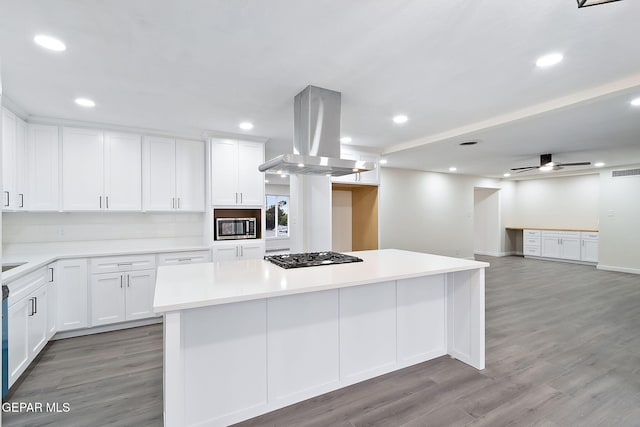 kitchen with island exhaust hood, gas stovetop, wood-type flooring, a center island, and white cabinetry