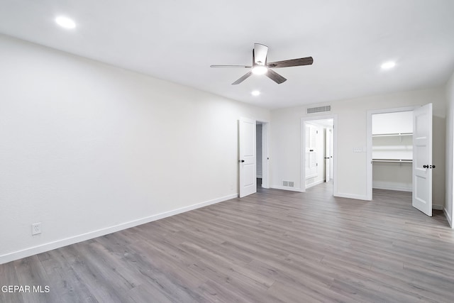 unfurnished bedroom featuring a walk in closet, light wood-type flooring, a closet, and ceiling fan