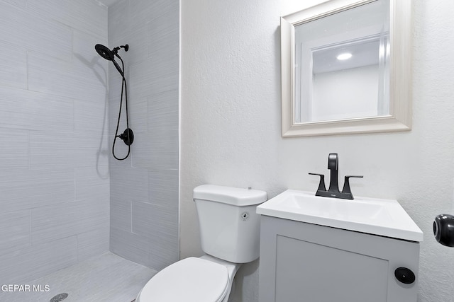 bathroom with a tile shower, vanity, and toilet