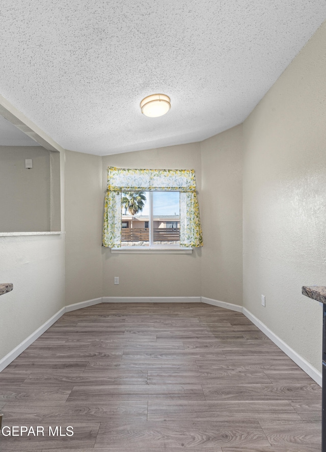 spare room featuring a textured ceiling, hardwood / wood-style floors, and vaulted ceiling