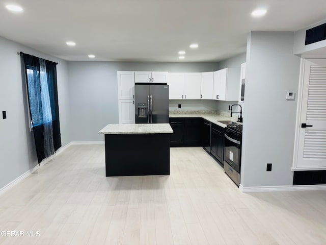 kitchen with appliances with stainless steel finishes, sink, light hardwood / wood-style flooring, white cabinets, and a kitchen island