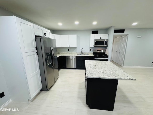 kitchen with white cabinetry, light stone countertops, sink, a kitchen island, and appliances with stainless steel finishes