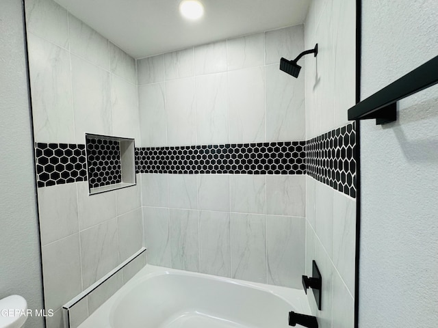 bathroom with toilet and tiled shower / bath