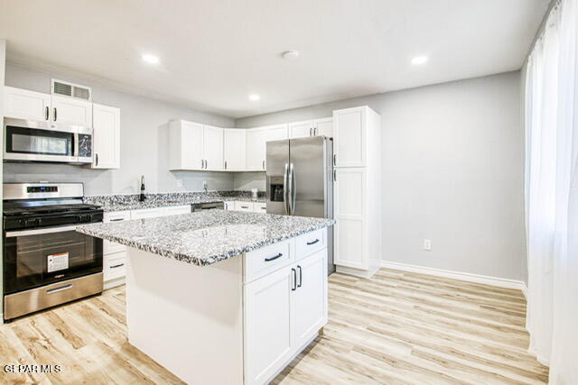 kitchen with light stone countertops, stainless steel appliances, a center island, light hardwood / wood-style floors, and white cabinetry