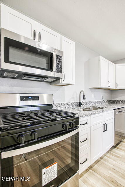 kitchen with light stone countertops, sink, appliances with stainless steel finishes, white cabinets, and light wood-type flooring