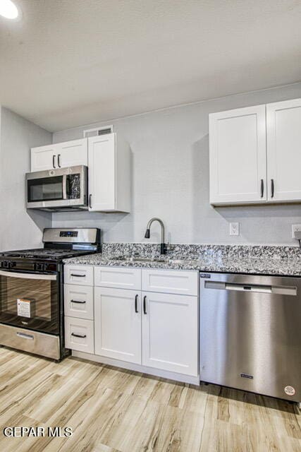 kitchen featuring light stone counters, white cabinetry, appliances with stainless steel finishes, and light hardwood / wood-style flooring