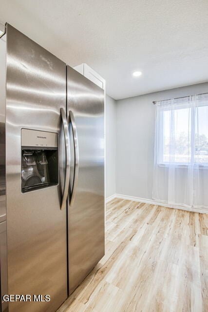 kitchen featuring stainless steel fridge, white cabinets, and light wood-type flooring