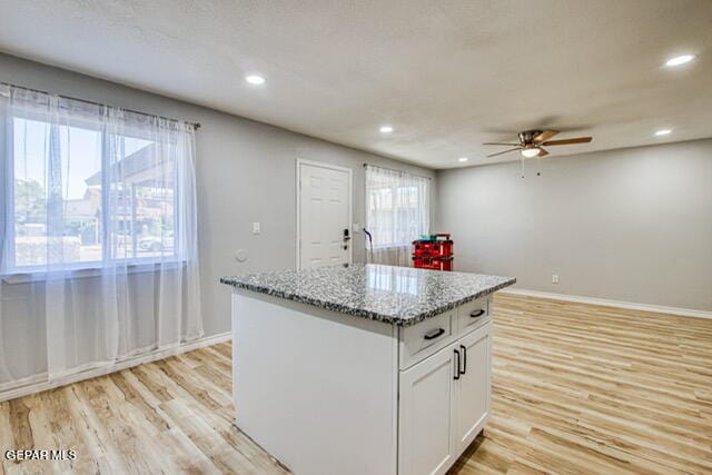 kitchen with a healthy amount of sunlight, light wood-type flooring, white cabinetry, and an island with sink