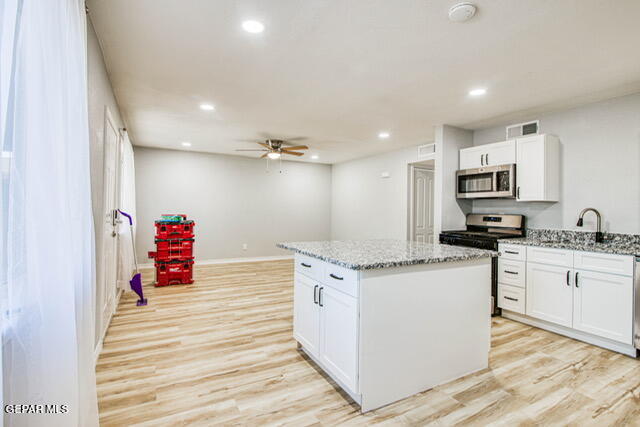 kitchen featuring white cabinets, a kitchen island, appliances with stainless steel finishes, light hardwood / wood-style floors, and light stone counters