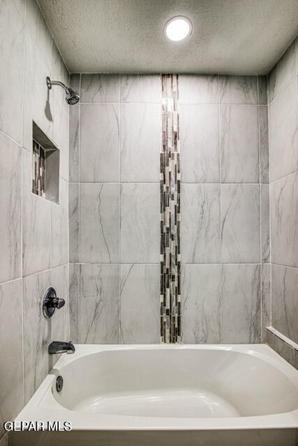 bathroom featuring a textured ceiling and tiled shower / bath combo