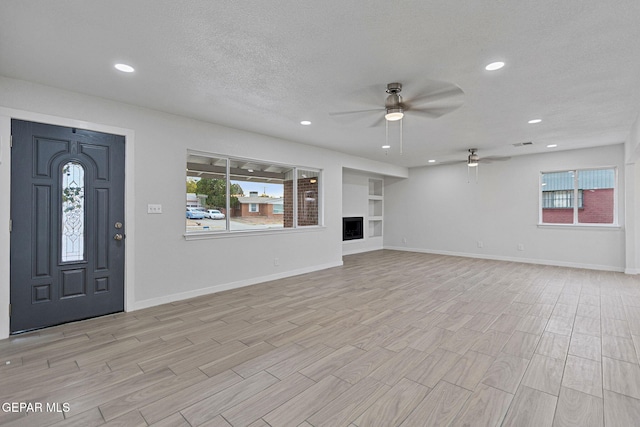 unfurnished living room featuring built in shelves, a textured ceiling, light hardwood / wood-style floors, and ceiling fan