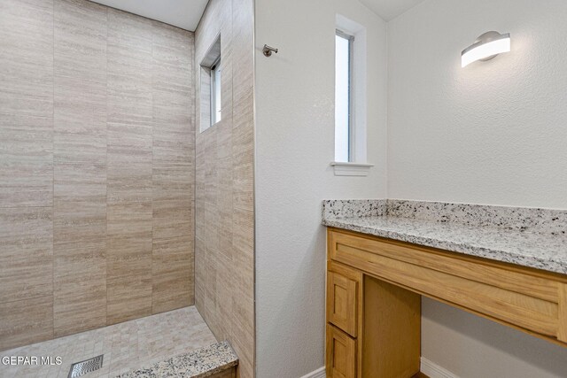 bathroom with vanity, tiled shower, and a wealth of natural light