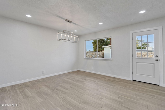 unfurnished dining area featuring plenty of natural light, a textured ceiling, and light hardwood / wood-style flooring