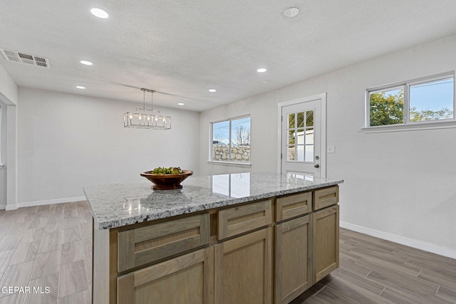 kitchen with a textured ceiling, a center island, light hardwood / wood-style floors, and hanging light fixtures