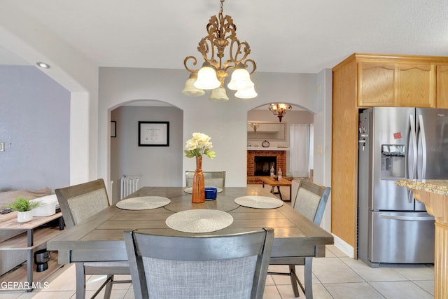 dining area with a chandelier, light tile patterned floors, and a brick fireplace