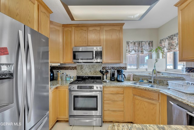 kitchen with light brown cabinetry, tasteful backsplash, light stone counters, stainless steel appliances, and sink