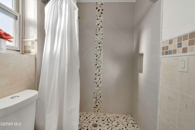 bathroom with a shower with shower curtain, toilet, and tile walls